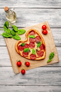 salam ve taze fesleğen yaprakları ile peynir kalp pizza ahşap arka plan üzerinde olgun kiraz domates ile zanaat kağıt üzerinde 