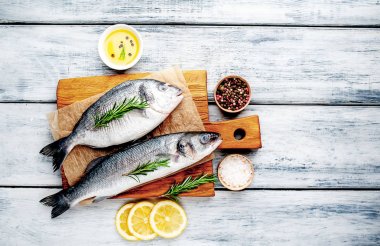 Ahşap doğrama tahtası üzerinde limon dilimleri ve biberiye dalları ile çiğ balık