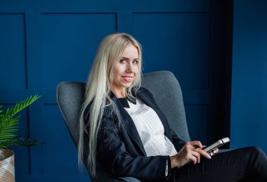 Not defteri tutan ve gri koltukta oturan sarışın genç kadın. 