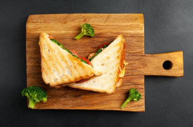 Ahşap doğrama tahtasında jambon, taze brokoli ve peynirile taze ızgara sandviçler
