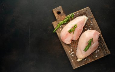 Ahşap doğrama tahtası üzerinde tuz ve biberiye dalları ile Çiğ tavuk fileto