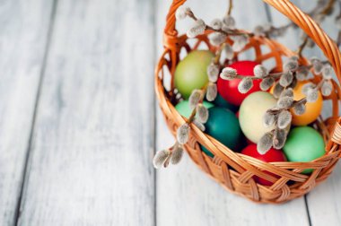 Beyaz ahşap arka planda renkli Paskalya yumurtaları ve kedi söğüt dalları ile sepet