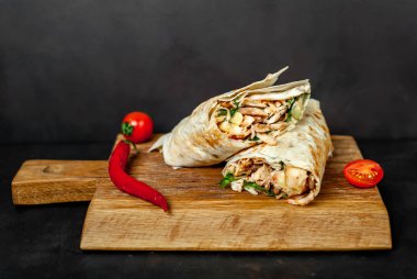 Geleneksel Meksika burrito tavuk ve sebze ile sarılmış ahşap doğrama tahtası üzerinde olgun domates ile servis 
