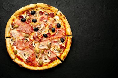Siyah taş arka plan üzerinde mantar, domates, zeytin ve jambon ile taze ev yapımı pizza