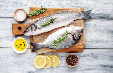 Ahşap doğrama tahtası üzerinde limon dilimleri ve biberiye dalları ile çiğ balık