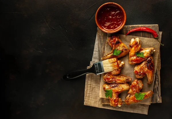 Siyah taş arka planda kesme tahtasında maydanoz ile barbekü sosu ızgara tavuk kanatları