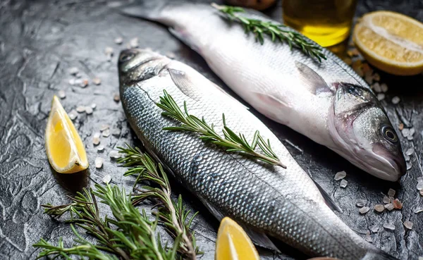 Siyah taş arka plan üzerinde limon, baharat ve biberiye dalları ile çiğ balık