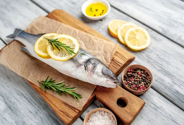 Ahşap doğrama tahtası üzerinde limon dilimleri ve biberiye dalları ile çiğ balık