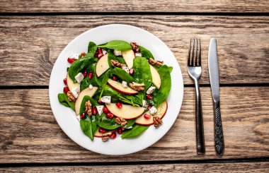 Ahşap arka plan üzerinde ıspanak yaprakları, peynir, nar tohumu, elma dilimleri ve fındık ile taze salata 