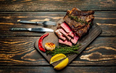 Taze kavrulmuş biftek ahşap doğrama tahtası üzerinde limon dilimleri ve ızgara sarımsak ile servis
