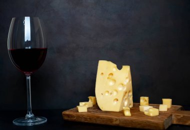Ahşap tahta üzerinde Maasdam peynirsiyah taş arka plan üzerinde kırmızı şarap ile servis 