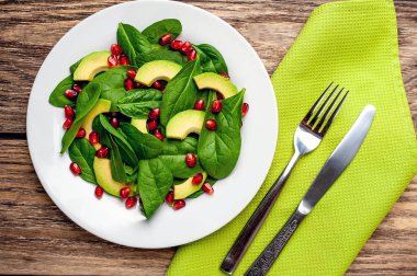 Ahşap masada ıspanak yaprakları, avokado dilimleri ve nar taneleri ile taze yeşil salata 
