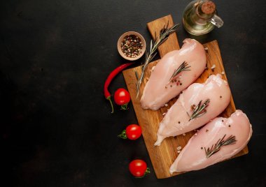 Ahşap doğrama tahtasında tuz, biberiye dalları ve zeytinyağı şişesi ile çiğ tavuk fileto