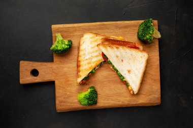 Ahşap doğrama tahtasında jambon, taze brokoli ve peynirile taze ızgara sandviçler