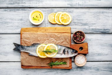 Ahşap doğrama tahtası üzerinde limon dilimleri ve biberiye dalları ile çiğ balık