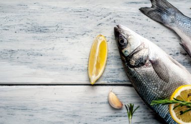Gri ahşap arka plan üzerinde limon dilimleri ve biberiye dalları ile çiğ balık
