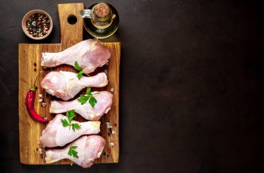 Siyah taş arka plan üzerinde ahşap doğrama tahtası üzerinde baharat, tuz, maydanoz yaprakları ve yağ şişesi ile Tavuk bacakları