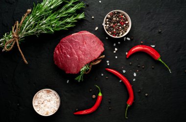 Siyah taş arka plan üzerinde yeşil biberiye dalları ve baharatlar ile Çiğ biftek 