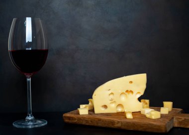 Ahşap tahta üzerinde Maasdam peynirsiyah taş arka plan üzerinde kırmızı şarap ile servis 