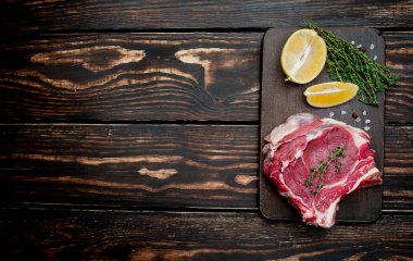 Ahşap arka plan üzerinde biberiye ve limon dilimleri ile Çiğ yağ domuz biftek 