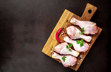 Ahşap doğrama tahtası üzerinde baharat, biber ve maydanoz yaprakları ile Tavuk bacakları 