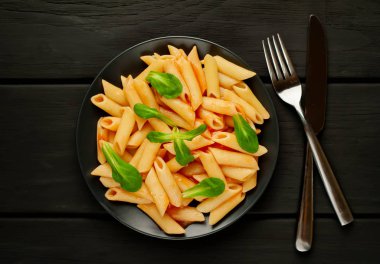 taş siyah arka plan üzerinde yeşil yaprakları ile servis domates soslu makarna