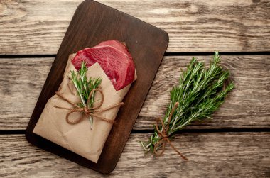 Ahşap doğrama tahtası üzerinde biberiye dalları ile zanaat kağıt sarılmış çiğ sığır eti biftek