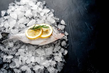 Soğuk ezilmiş buz yığını üzerinde limon dilimleri ve biberiye ile taze balık yakın görünümü