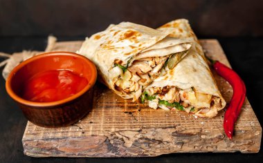 Ahşap doğrama tahtası üzerinde baharatlı sos ile tavuk ve sebze ile sarılmış geleneksel Meksika burrito 