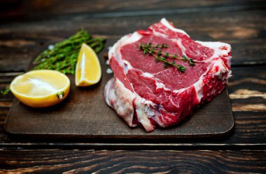 Ahşap arka plan üzerinde biberiye ve limon dilimleri ile Çiğ yağ domuz biftek 