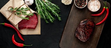 Izgara biftek ve çiğ et siyah taş arka plan üzerinde zanaat kağıt sarılmış