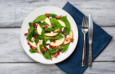 Ahşap arka plan üzerinde ıspanak yaprakları, peynir, nar tohumu, elma dilimleri ve fındık ile taze salata 