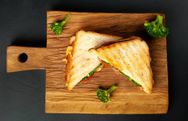 Ahşap doğrama tahtasında jambon, taze brokoli ve peynirile taze ızgara sandviçler