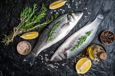 Siyah taş arka plan üzerinde limon, baharat ve biberiye dalları ile çiğ balık