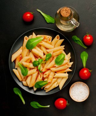 domates soslu makarna, yeşil yapraklar ve taş siyah arka plan üzerinde olgun domates