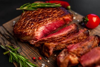 Ahşap doğrama tahtası üzerinde biberiye dalları ile dilimlenmiş orta nadir sığır eti biftek yakın görünümü