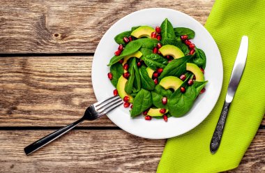 Ahşap masada ıspanak yaprakları, avokado dilimleri ve nar taneleri ile taze yeşil salata 