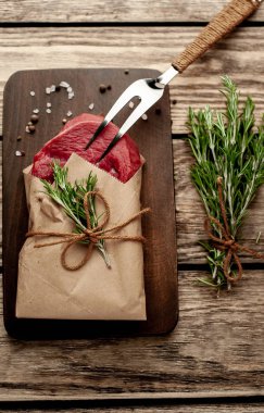 Ahşap doğrama tahtası üzerinde biberiye dalları ile zanaat kağıt sarılmış çiğ sığır eti biftek