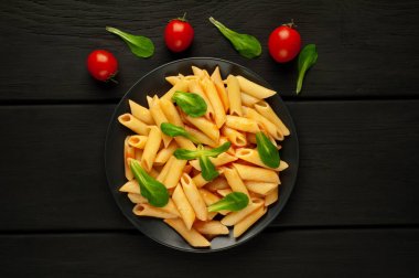 domates soslu makarna, yeşil yapraklar ve taş siyah arka plan üzerinde olgun domates