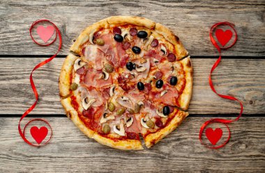 Kırmızı kurdeleler ve kalpler ile ahşap arka plan üzerinde mantar, domates, zeytin ve jambon ile taze ev yapımı pizza