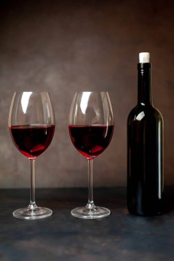 Siyah arka planda iki bardak kırmızı şarap ve şarap şişesi