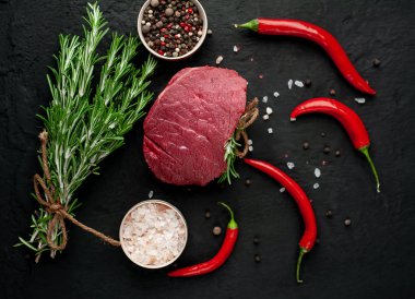 Siyah taş arka plan üzerinde yeşil biberiye dalları ve baharatlar ile Çiğ biftek 