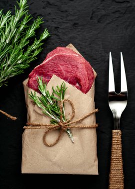 Çiğ sığır eti biftek taş arka plan üzerinde biberiye dalları ile zanaat kağıt sarılmış 