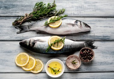 Gri ahşap arka plan üzerinde limon dilimleri ve biberiye dalları ile çiğ balık