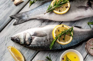 Gri ahşap arka plan üzerinde limon dilimleri ve biberiye dalları ile çiğ balık