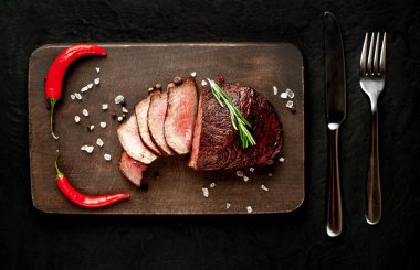 Siyah taş arka plan üzerinde baharat ve biberiye dal ile Taze ızgara biftek