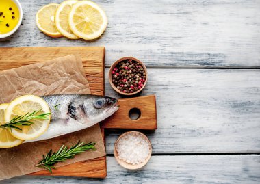 Ahşap doğrama tahtası üzerinde limon dilimleri ve biberiye dalları ile çiğ balık