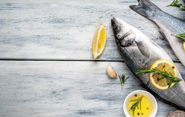 Gri ahşap arka plan üzerinde limon dilimleri ve biberiye dalları ile çiğ balık