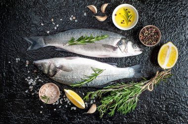 Siyah taş arka plan üzerinde limon, baharat ve biberiye dalları ile çiğ balık