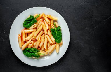 taş siyah arka plan üzerinde yeşil yaprakları ile servis domates soslu makarna